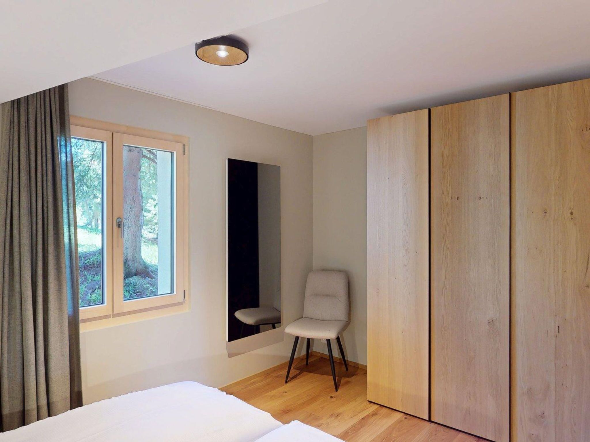 Un dormitorio con cama, una silla, armario, ventana y espejo.