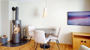 Uma sala de estar moderna com uma lareira a lenha, uma mesa de jantar redonda com cadeiras, um lustre e um quadro na parede.
