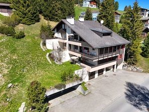 A modern two-story house with a sloped roof, a balcony, and a small garden area.