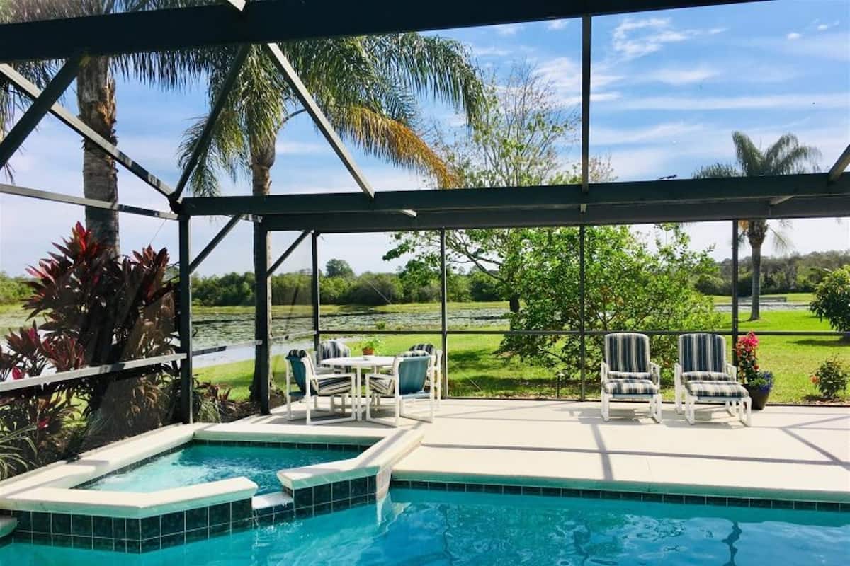 A pool area with a covered patio, outdoor seating, and a view of a golf course.