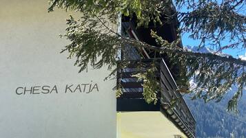 Un edificio con el nombre 'CHESA KATJA' en su fachada, una puerta marcada con el número '6', y una vista de montañas nevadas al fondo.
