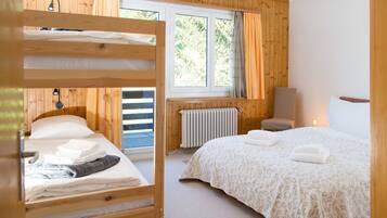 Una habitación con una litera, una cama individual, una silla, un radiador y una ventana con cortinas.