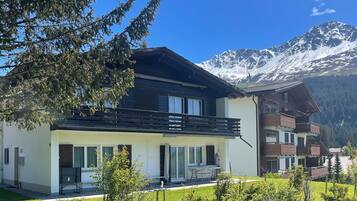 Ein modernes, zweistöckiges Chalet mit Balkon, vor einer Kulisse schneebedeckter Berge.