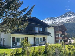 Una moderna chalet de dos pisos con balcón, frente a imponentes montañas nevadas.