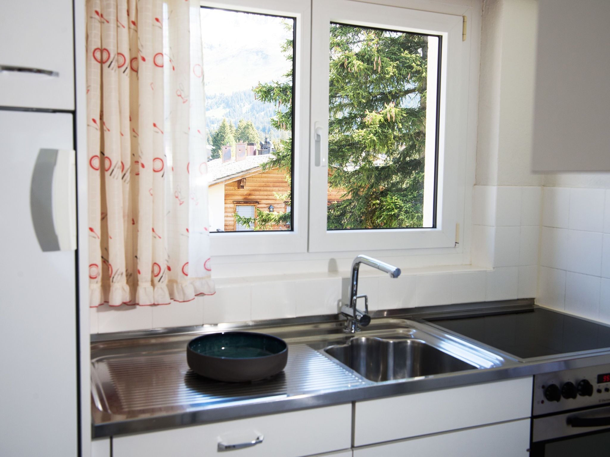 Una cocina con un lavamanos de acero inoxidable, un bol y una ventana que ofrece vistas a árboles y un edificio.