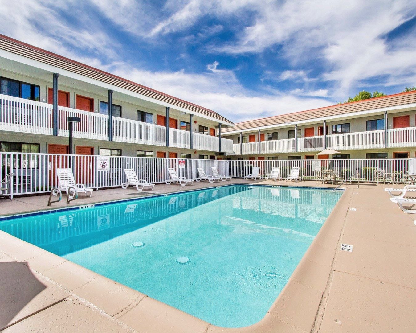 Ein Hotel mit Schwimmbad, weißen Balkonen und Liegestühlen.