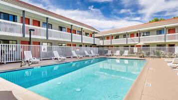 A hotel with a swimming pool, white balconies, and lounge chairs.
