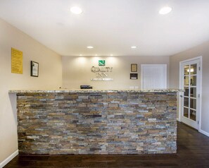 A reception area with a stone counter, a sign for Quality Inn, and a door to the right. - Quality Inn Flagstaff East I-40 (Flagstaff)