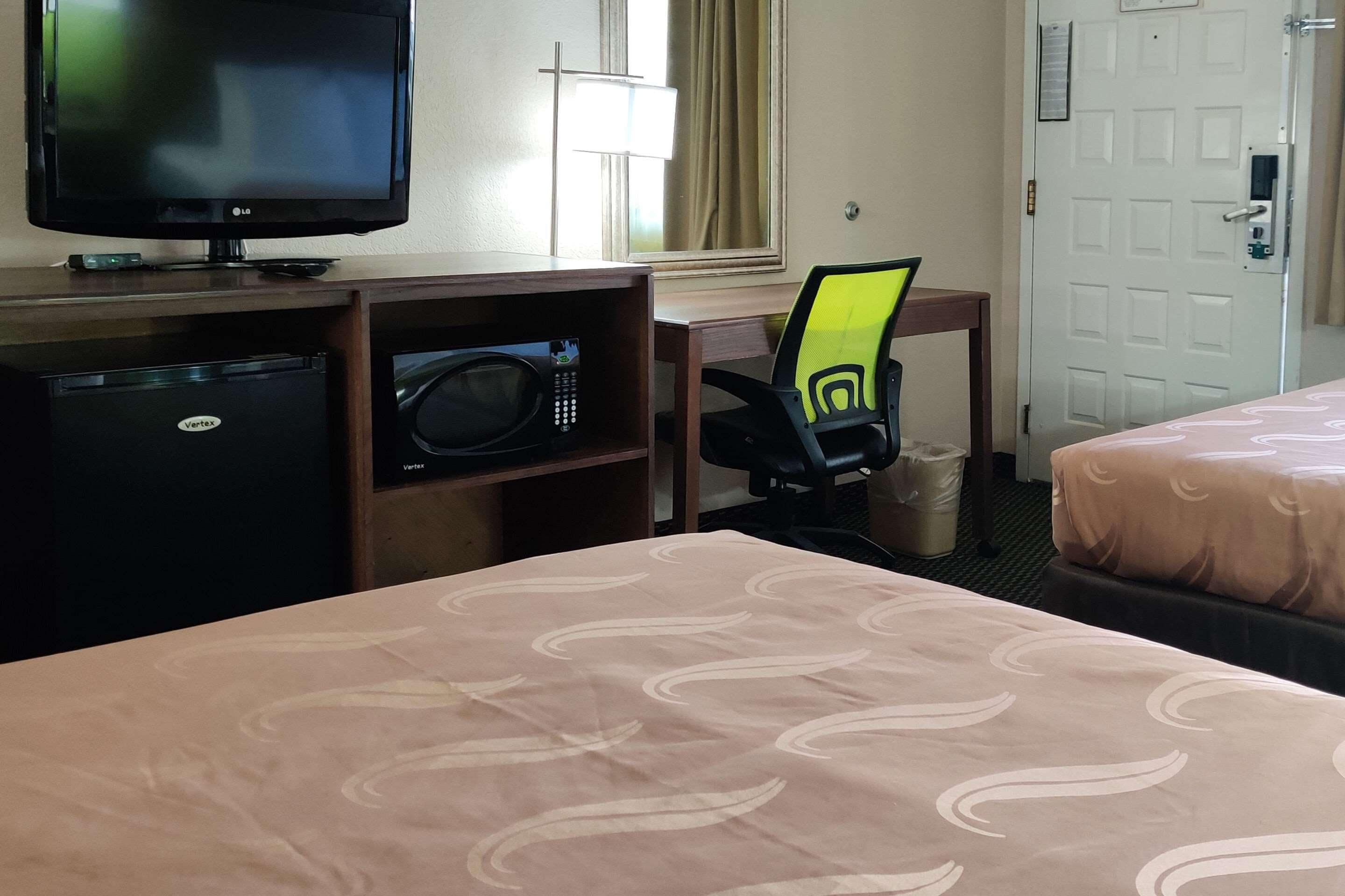 A hotel room with a bed, a desk with a computer, a television, a refrigerator, and a microwave.