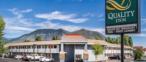 A Quality Inn with a signboard, a parking lot, and a mountainous backdrop.