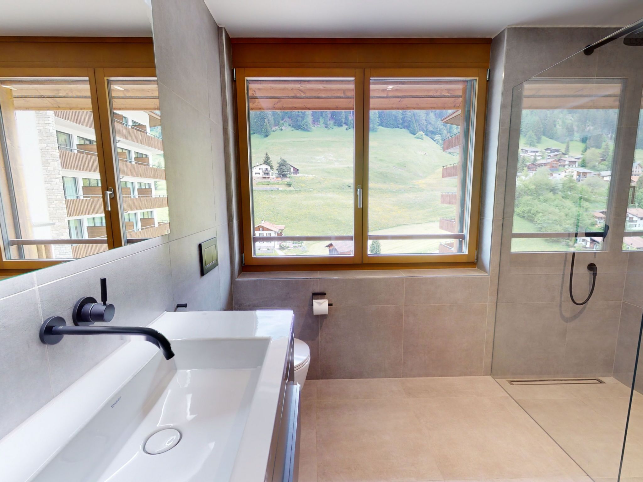 Un baño moderno con bañera, inodoro y ducha, grandes ventanales con vistas a un área residencial.