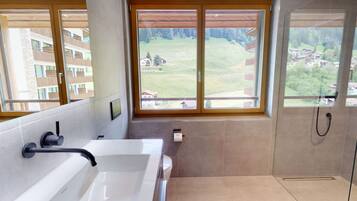 Un baño moderno con bañera, inodoro y ducha, grandes ventanales con vistas a un área residencial.