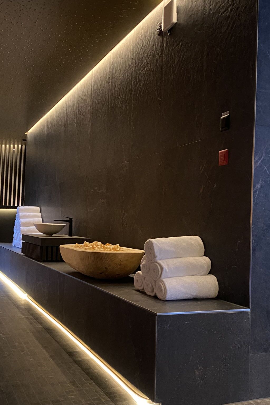 Un bagno moderno con una parete scura, una ciotola di legno e asciugamani ordinatamente piegati.