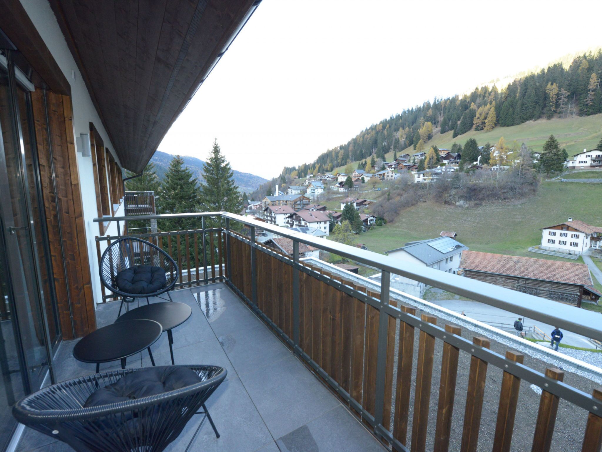 Ein Balkon mit Blick auf ein Dorf, ein Stuhl und ein Tisch.