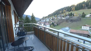 Ein Balkon mit Blick auf ein Dorf, ein Stuhl und ein Tisch.
