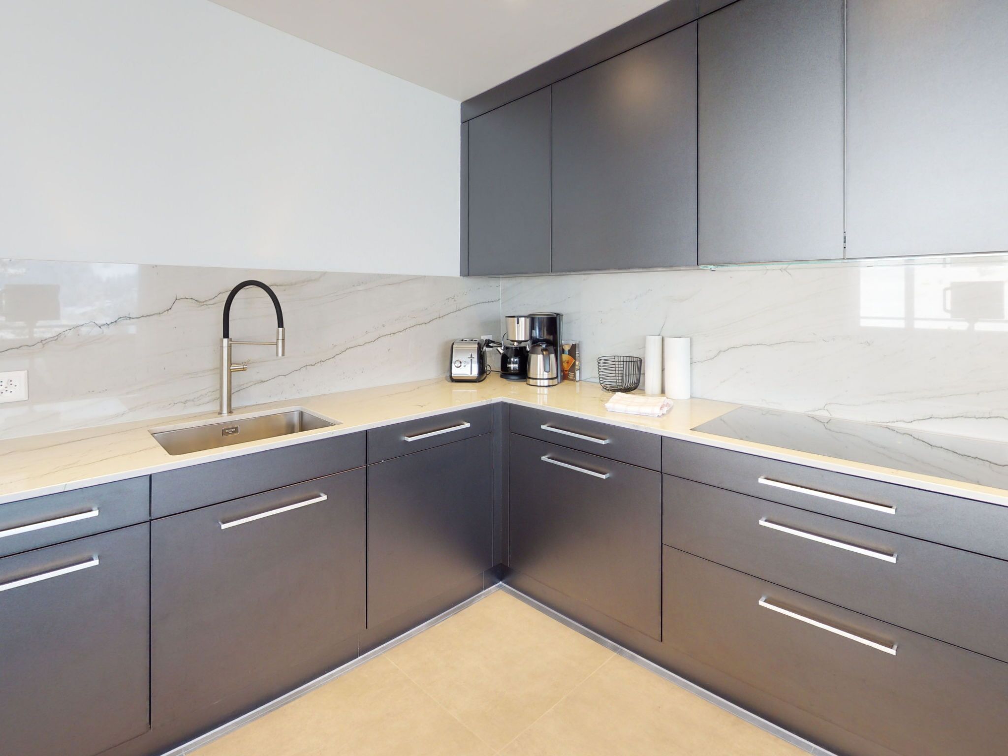 A modern kitchen with grey cabinets, a marble backsplash, and a stainless steel sink.
