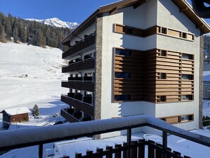 Un immeuble moderne à plusieurs étages, doté de balcons, qui se dresse sur fond de montagnes enneigées.