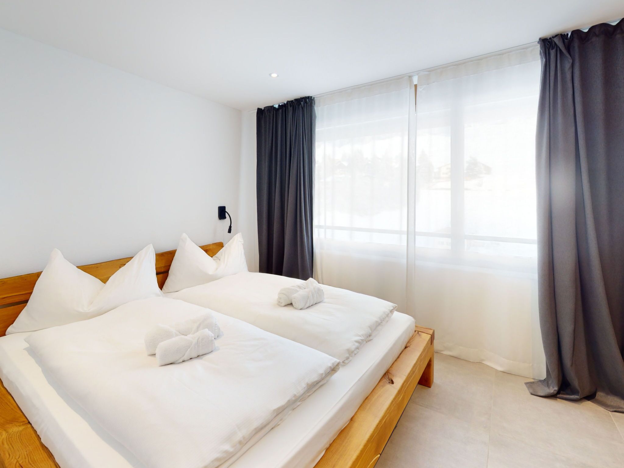 Ett hotellrum med två sängar, vita sängkläder, en sänggavel i trä, ett stort fönster med gardiner och ett vägguttag.