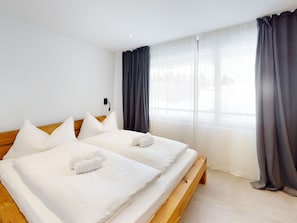 A hotel room with two beds, white bedding, a wooden headboard, a large window with curtains, and a wall-mounted power outlet. - 1303 Krone Churwalden by Interhome (Churwalden)