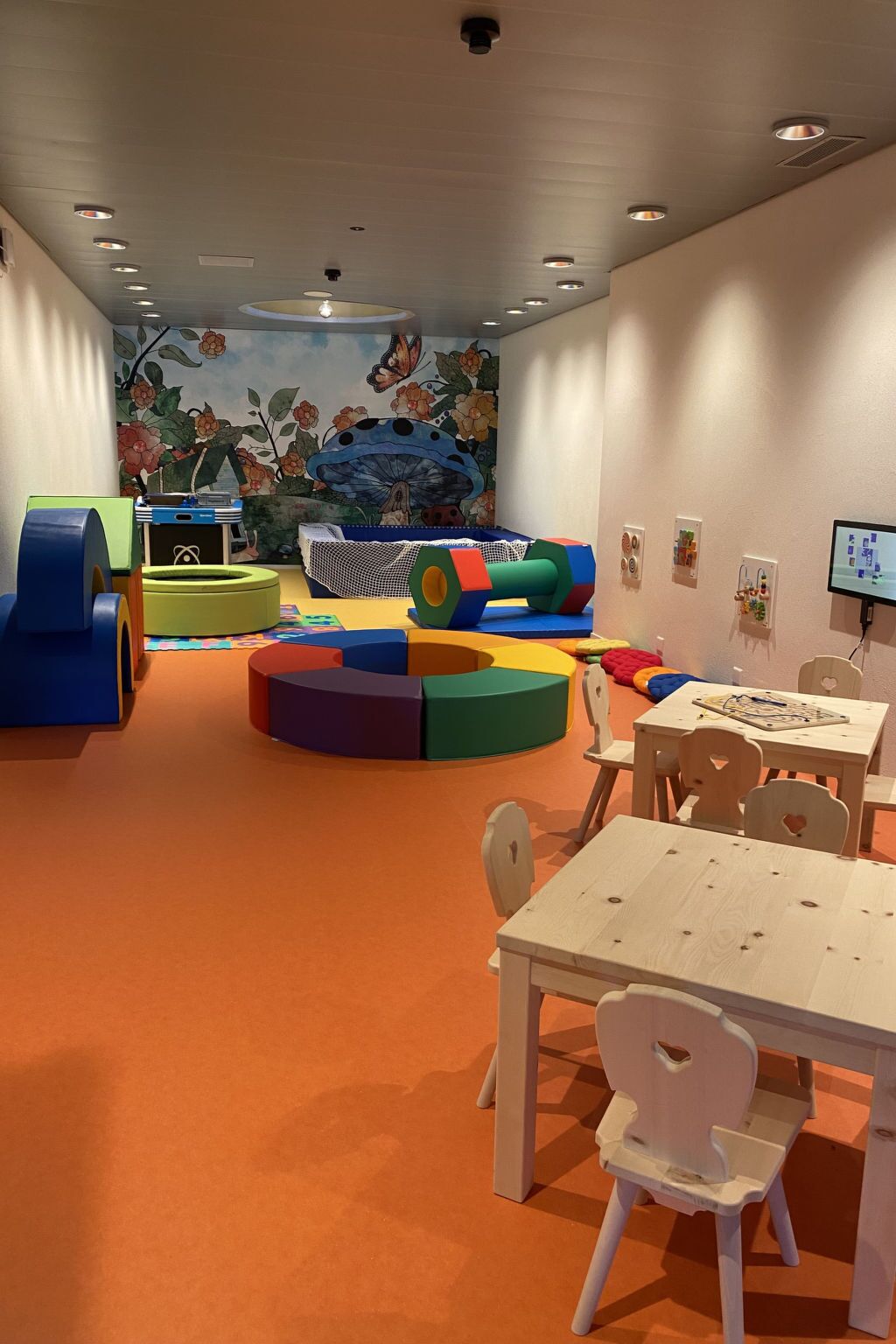 A children's play area with colorful play structures, a mural, and a table with chairs.