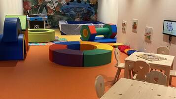 A children's play area with colorful play structures, a mural, and a table with chairs.
