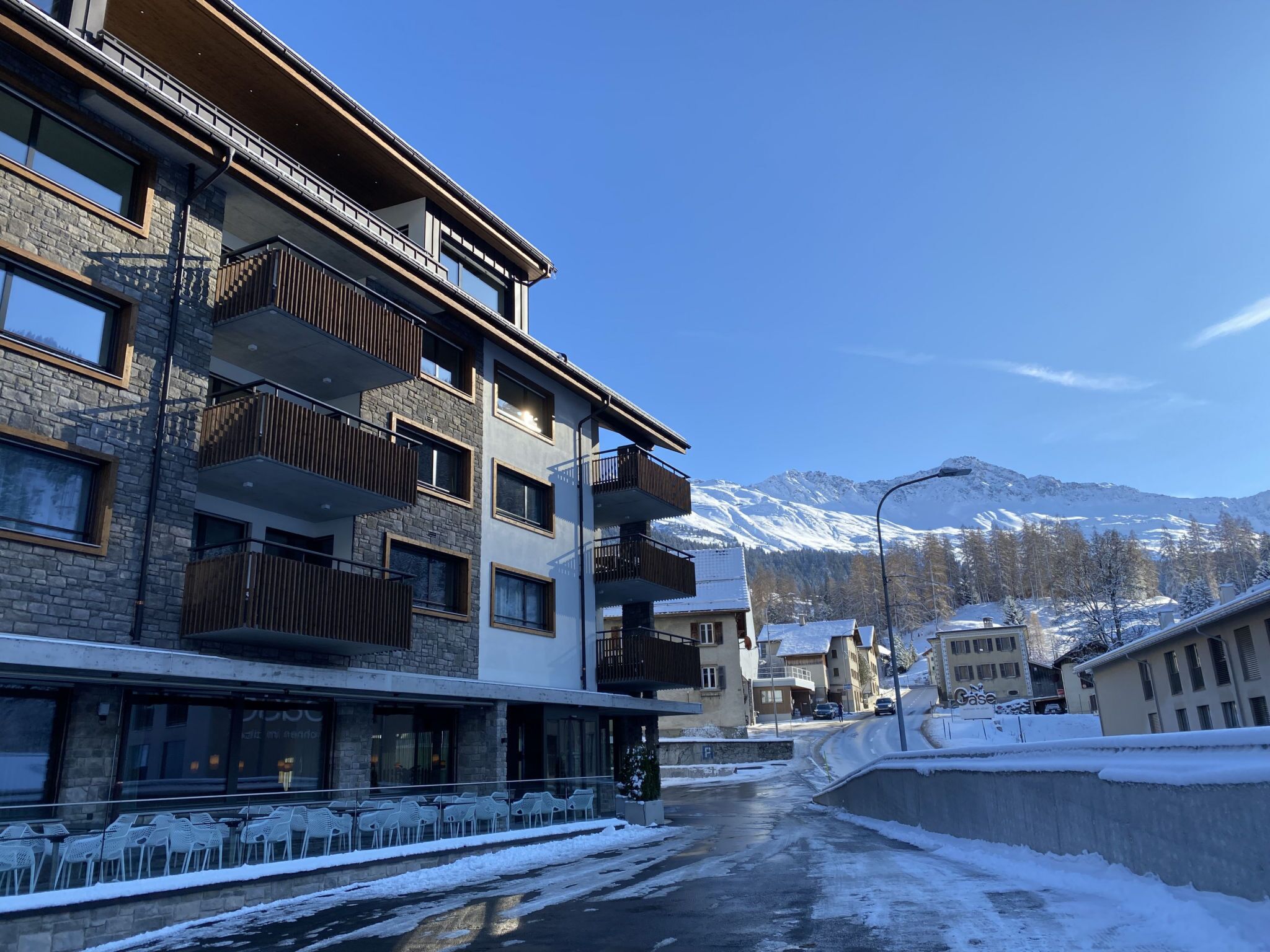 Ein mehrstöckiges Gebäude mit Balkonen, eine verschneite Straße und Berge im Hintergrund.