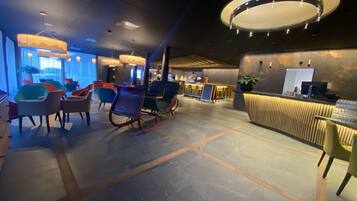 A modern hotel lobby with a reception desk, seating area, and a bar.