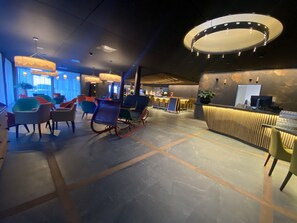 Un hall d’hôtel moderne comprenant un comptoir d’accueil, un espace salon et un bar.