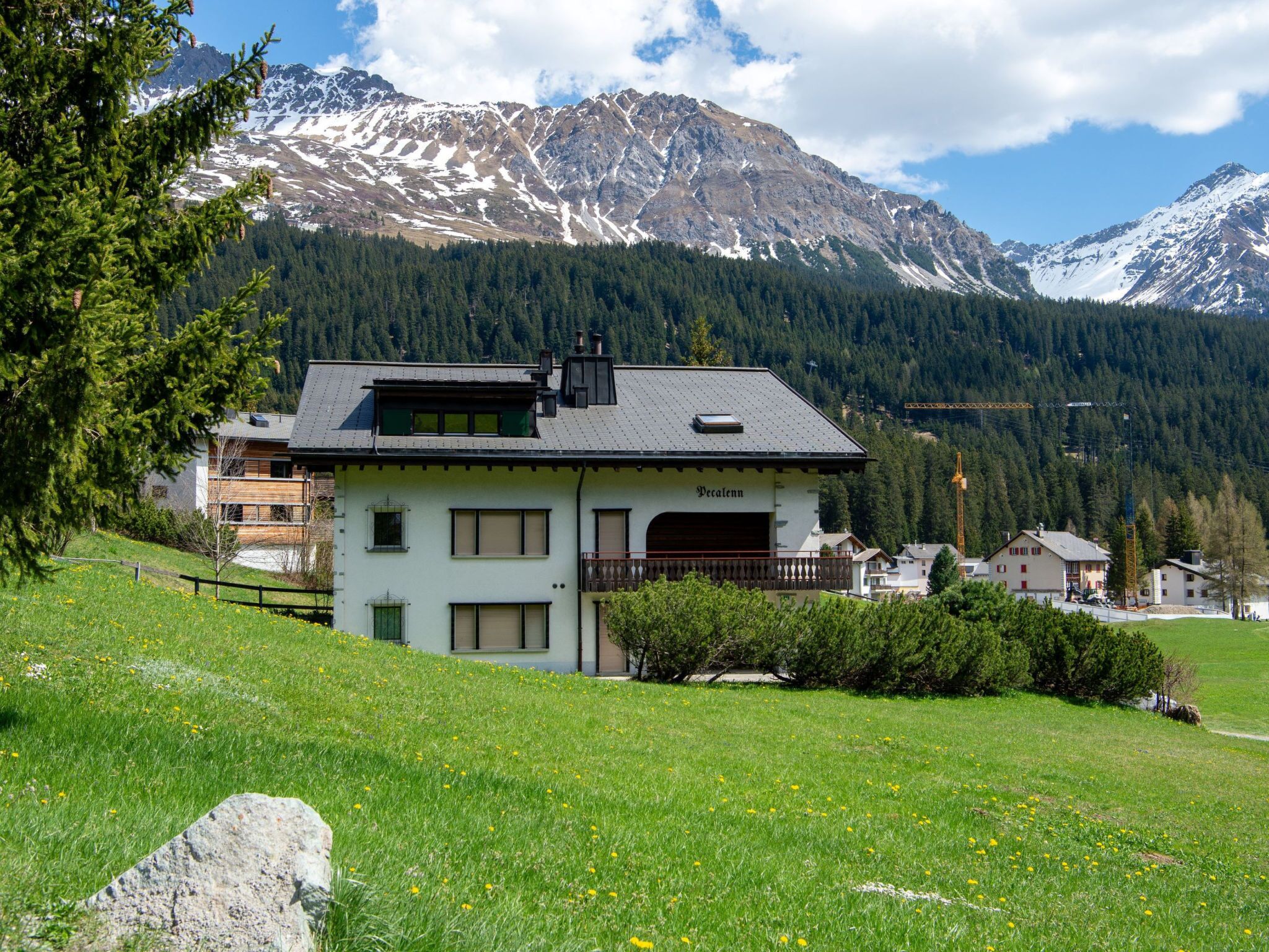 Ein zweistöckiges Gebäude mit geneigtem Dach, einem Balkon und Blick auf schneebedeckte Berge im Hintergrund.