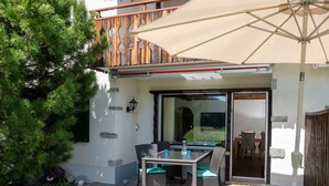 An outdoor patio with a table and chairs, a wooden fence, and a potted tree. - 1507 Davos Lai Valbella by Interhome (Valbella)