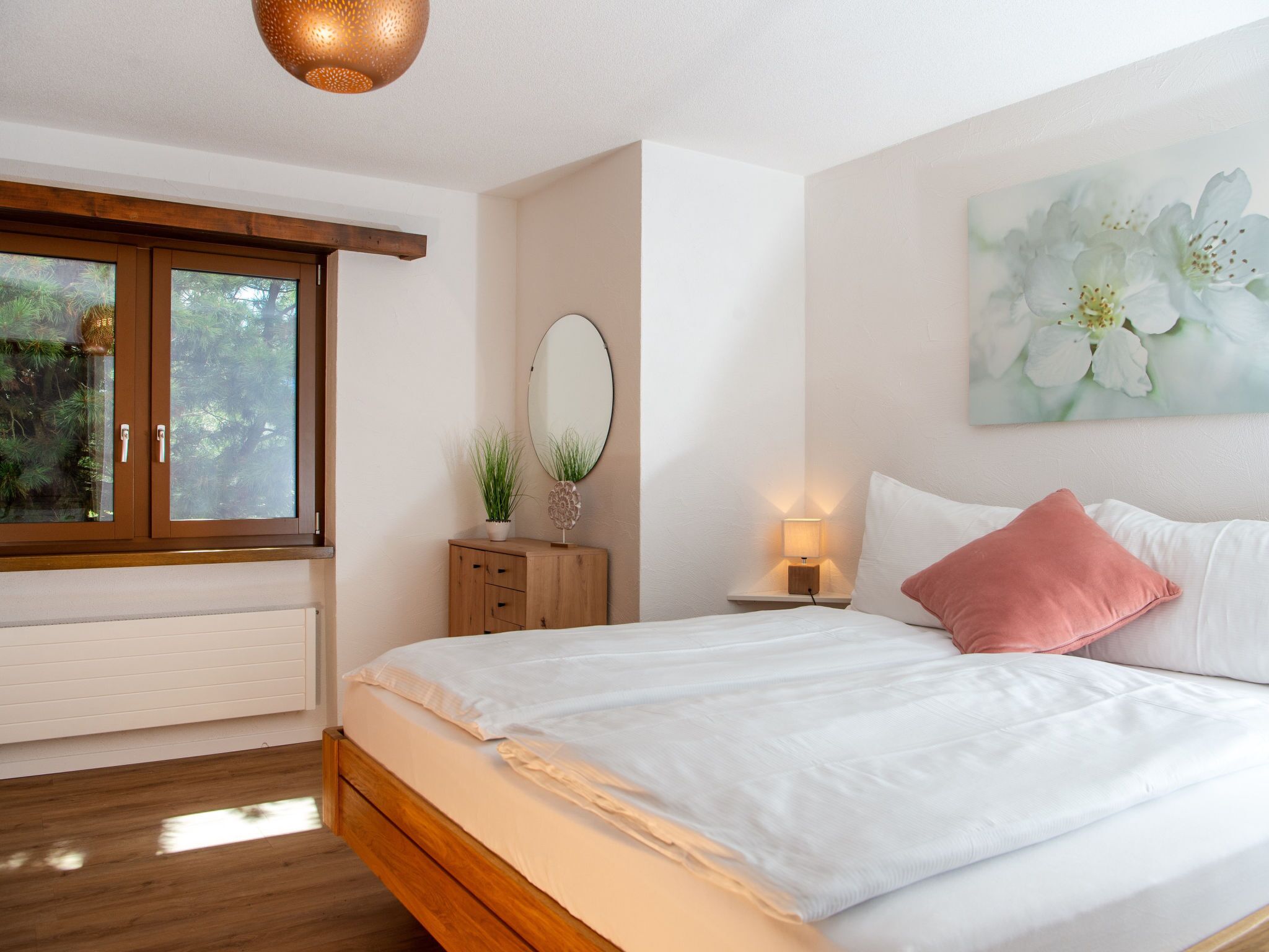 Une chambre à coucher avec un grand lit, une fenêtre, une table de chevet avec une lampe et un miroir fixé au mur.