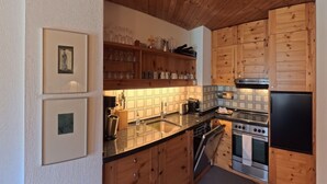 Una cocina con armarios de madera, un lavamanos de acero inoxidable y un refrigerador negro.