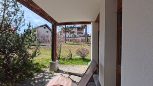 Un espacio al aire libre techado con un banco, un poste de madera y vista a un edificio al fondo.