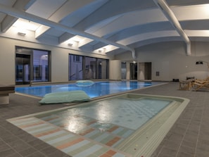 Une piscine intérieure avec un sol carrelé, un espace détente avec des fauteuils et une grande fenêtre.