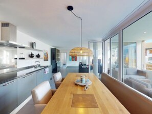 Een moderne keuken met een houten eettafel, een hanglamp en uitzicht op de stad door grote ramen.