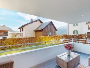Een balkon met rieten meubilair, een vaas met bloemen en uitzicht op huizen en bergen.