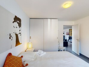 A hotel room with a bed, a nightstand, a lamp, a wardrobe, and a wall decoration. - 1901 Sot by Interhome (Lantsch)