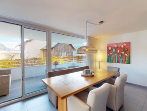 Un comedor moderno con una mesa de madera, sillas blancas y vistas a un paisaje montañoso a través de amplios ventanales correderas.