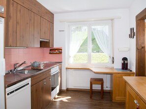 A kitchen with wooden cabinets, a sink, a kettle, and a window with a view of greenery. - 1611 Pianura Crapera by Interhome (Lenzerheide)