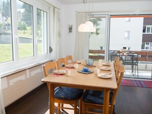 Een eethoek met een tafel gedekt voor vier personen, stoelen, een hanglamp en uitzicht op een balkon met tuinmeubilair.