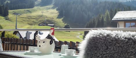 A balcony with a view of a mountainous landscape, a white teapot, two cups, and a furry object in the foreground.