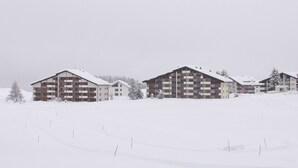 A snow-covered landscape with two multi-story buildings, likely a hotel or resort, with balconies and a flat roof. - 1401 Heimberg by Interhome (Parpan)