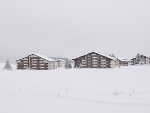 Un paysage enneigé avec deux bâtiments à plusieurs étages, probablement un hôtel ou un complexe touristique, dotés de balcons et d’un toit plat.