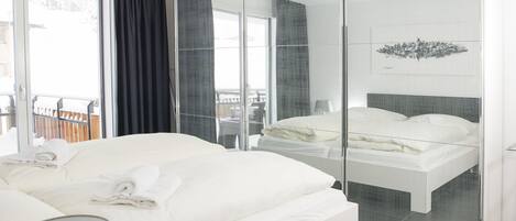 A modern hotel room with a large bed, a separate sleeping area, a balcony with a view, and a cityscape artwork on the wall.