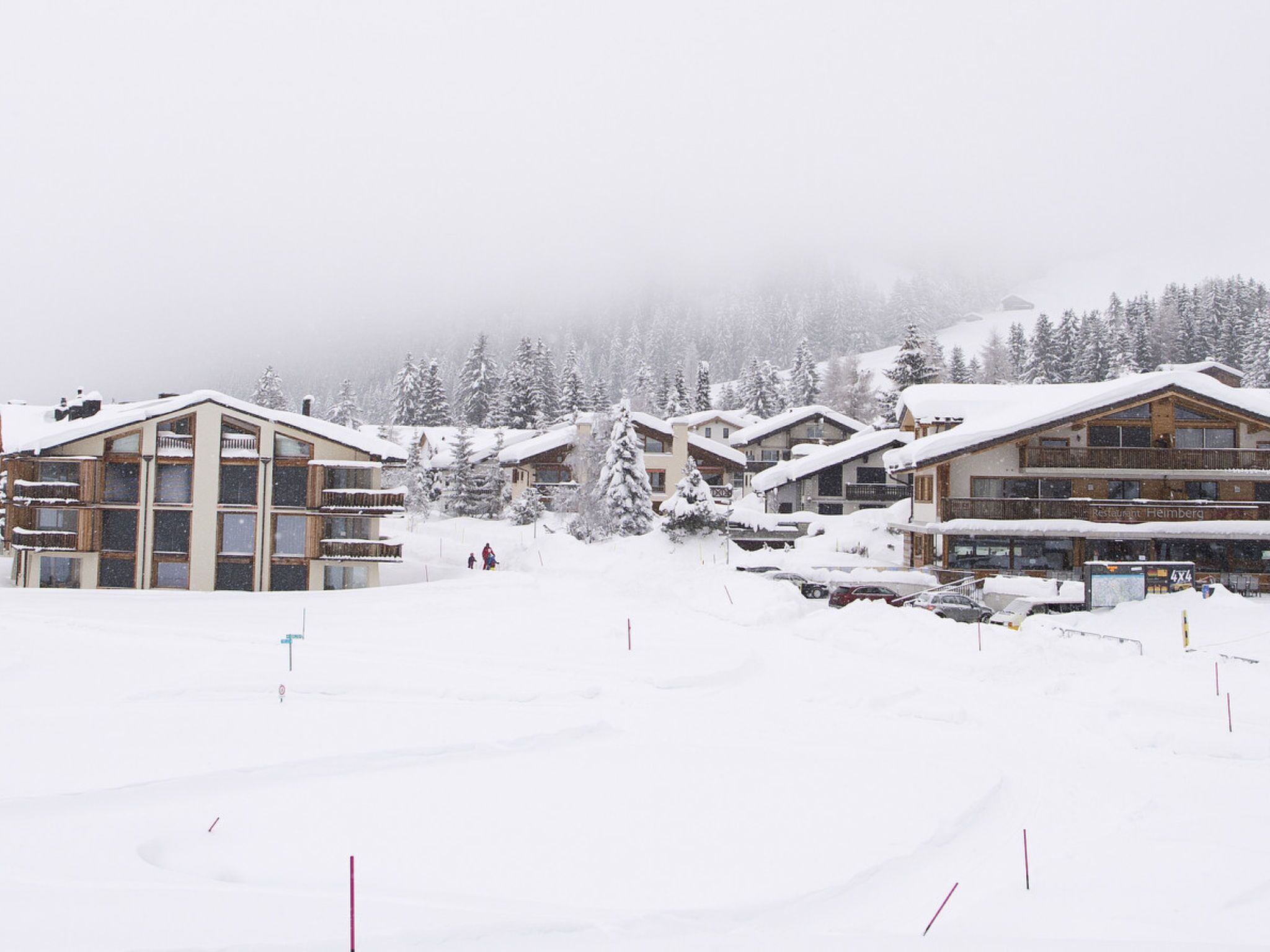 A snow-covered ski resort with multiple chalet-style buildings, a restaurant, and a parking area.