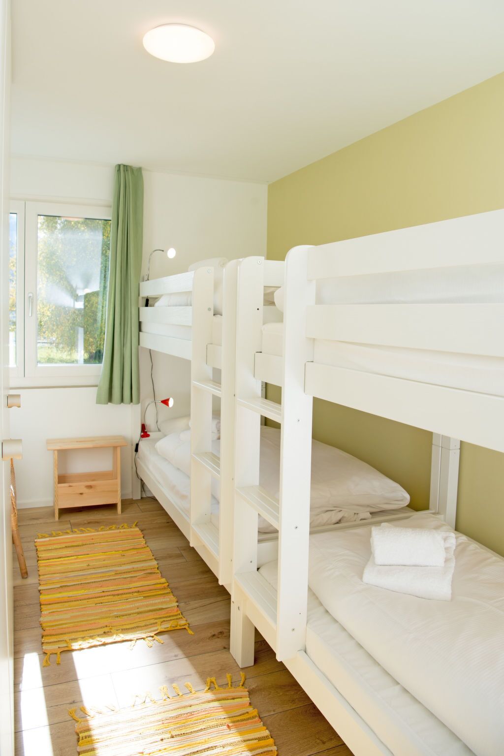 Ein Zimmer mit Etagenbetten, einem kleinen Nachttisch, einer Lampe und einem Fenster mit Vorhängen.
