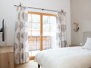 Un dormitorio con cama, cómoda de madera, televisor y ventana con cortinas.