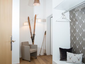 Una habitación con una silla a cuadros, esquíes apoyados en la pared, una lámpara y un perchero con un cortinero estampado con motivos de corazón.