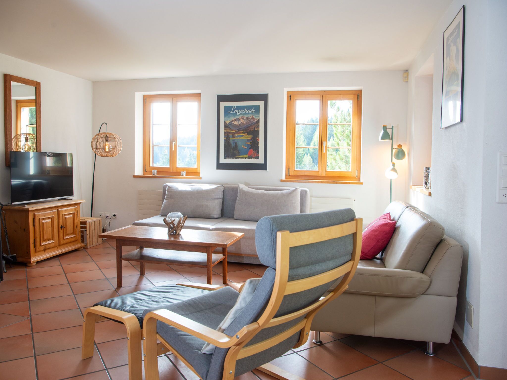 Un salon avec un canapé, un fauteuil, une table basse, un téléviseur et une affiche accrochée au mur.