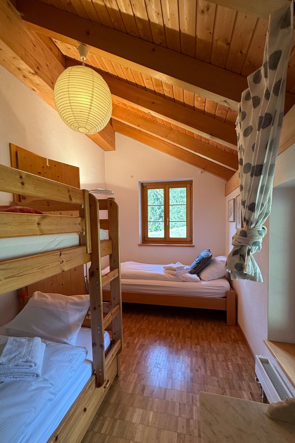 Una habitación pequeña y acogedora con una litera, una cama individual, una ventana y una lámpara colgante.